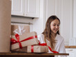 © Jastina - Pretty Caucasian teenage girl packing Christmas boxes in bright kitchen with red and white ribbons