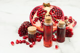 Fototapeta Tulipany - bottles of essential oil and ripe pomegranate fruit on a marble background. concept of moisturizing, aromatherapy, anti-stress effect.