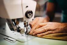 Fashion Designer Sewing Clothes On Machine In Workshop