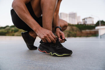 Wall Mural - Black sportswoman tying shoelaces while working out on parking