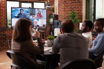 Wall Mural - Diverse businessteam discussing management strategy with remote entrepreneurs during online videocall meeting working in startup company office. Business call conference on monitor
