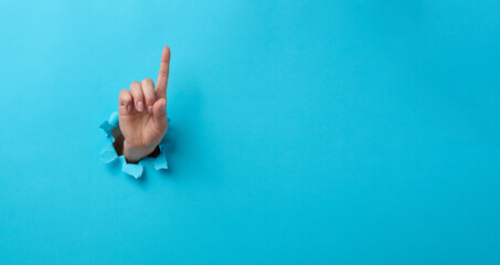 female hand sticking out of a torn hole in a blue paper background, attention gesture. Place for an inscription, banner