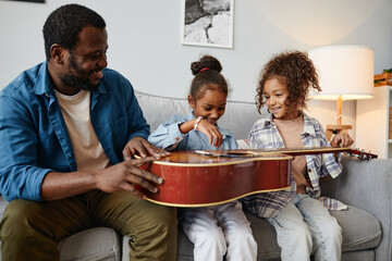 Wall Mural - Portrait of happy African-American father playing with two cute girls at home