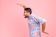 © khosrork - Side view of cheerful bearded man in blue casual shirt dancing, having fun and doing funny egyptian arm dance move, celebrating, rejoicing. Indoor studio shot isolated on pink background.