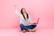 © khosrork - Extremely happy female sitting on floor with laptop yelling, celebrating her victory or success, wearing white casual style sweater. Indoor studio shot isolated on pink background.