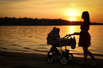 Canvas Print - Happy mother with baby in stroller walking near river at sunset