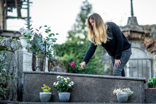 Blond Woman Putting Flower On Grave At Cemetery