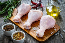 Raw Chicken Drumsticks On Cutting Board With Seasonings On Wooden Table
