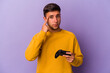 © Asier - Young caucasian man holding game controller isolated on purple background  pointing temple with finger, thinking, focused on a task.