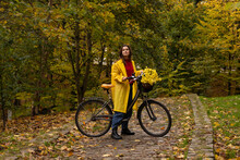 Woman Wearing Raincoat Standing With Flowers In Bicycle Basket