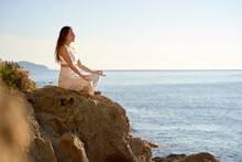 Sportswoman Meditating In Lotus Position On Rock At Sunset