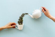 Female Hand Pours Tea Leaves From Teapot In Cup