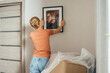 © Westend61 - Woman mounting picture frame on wall in new apartment