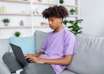 Canvas Print - Home schooling concept. Black teen guy using laptop pc for his online studies on couch indoors