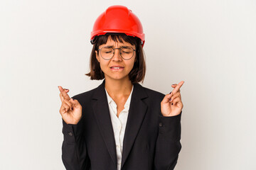 Wall Mural - Young architect woman with red helmet isolated on white background crossing fingers for having luck