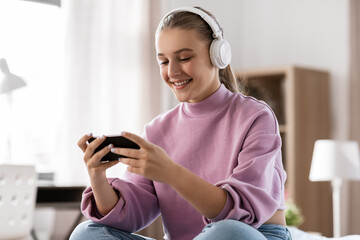 Wall Mural - technology and people concept - happy smiling girl in headphones with smartphone at home