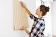 © Syda Productions - repair, improvement and renovation concept - happy smiling woman applying wallpaper to wall at home