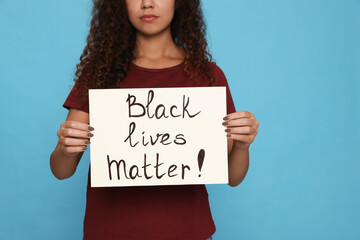 Wall Mural - African American woman holding sign with phrase Black Lives matter on light blue background, closeup. Racism concept