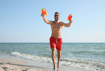 Wall Mural - Man with water guns having fun on beach