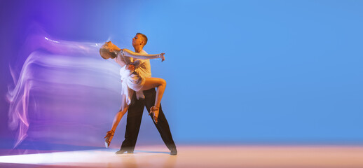 Young graceful dancers, flexible man and woman dancing ballroom dance isolated on gradient blue purple background in neon mixed light