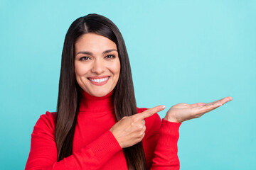 Poster - Photo of adorable shiny mature woman wear red sweater pointing finger holding arm empty space smiling isolated turquoise color background