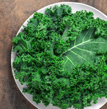 Fototapeta Kuchnia - Kale Salad. Fresh Green Kale vegetable leaves on white plate over wooden background, top view. Healthy eating vegetarian food concept..