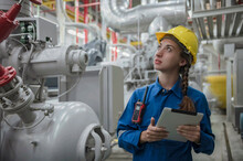 Female Engineer Smiling With Yellow Hard Hat Helmet And Holding Tablet Working Inside Factory