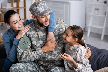 Canvas Print - Positive family sitting near man in military uniform on couch