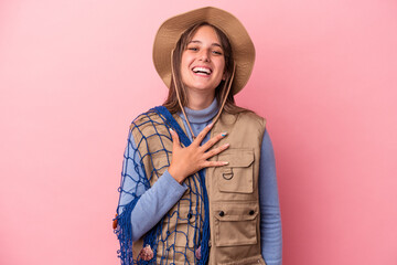 Wall Mural - Young caucasian fisherwoman holding a net isolated on pink background laughs out loudly keeping hand on chest.