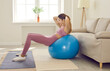© Studio Romantic - Woman having fitness workout at home. Young girl using exercise ball for abs training. Side view of happy lady holding hands behind head and doing sit ups on stability ball near sofa in living room