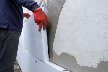 Construction worker installing styrofoam insulation sheets on house facade wall for thermal protection.