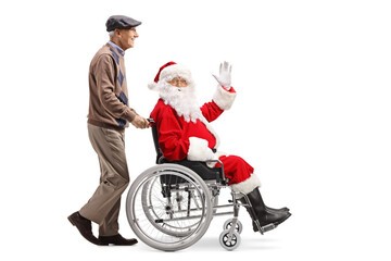 Wall Mural - Full length profile shot of an elderly man pushing santa claus in a wheelchair waving at camera