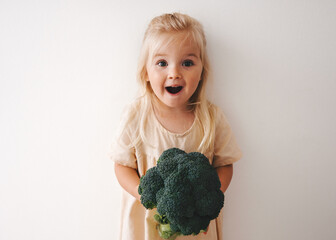 Wall Mural - Surprised girl with broccoli healthy food vegan child family lifestyle organic vegetables harvest natural vitamins plant based diet nutrition funny kid