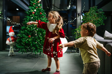 Overjoyed happy little girl and her brother playing with garland lights.