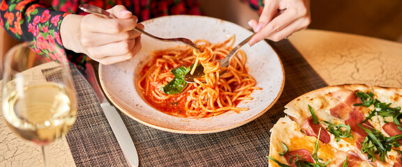 Wall Mural - Woman eats Italian pasta with tomato, meat. Close-up spaghetti Bolognese wind it around a fork with a spoon. Parmesan cheese