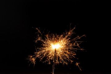 Horizontal conceptual close-up picture of an orange sparkler in action with lots of bright hot sparks flying in all directions on the black background