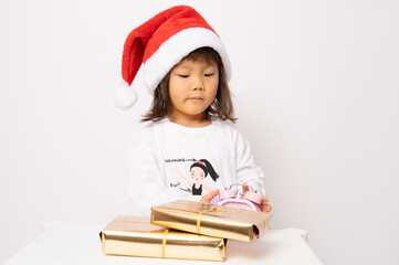 Wall Mural - Little asian girl in santa hat sitting with gift boxes isolated over white background.