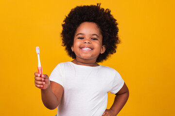 A little cute african american girl brushing her teeth, isolated over yellow background. Healthy teeth concept.