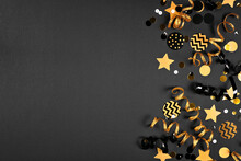 New Years Party Side Border With Glittery Black And Gold Streamers And Confetti. Top View On A Black Background.