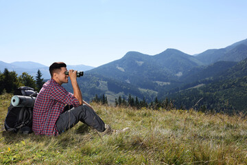 Canvas Print - Tourist with hiking equipment looking through binoculars in mountains