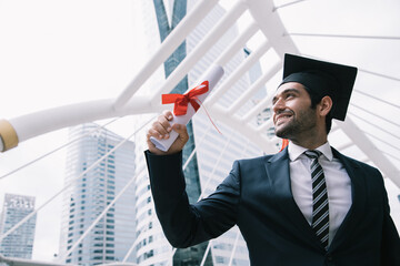 Handsome businessman wear graduation degree hat and selfie pictures while sits on stair near cityscape, business education concept