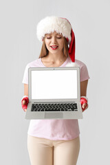 Wall Mural - Beautiful young woman in Santa hat and with laptop on grey background