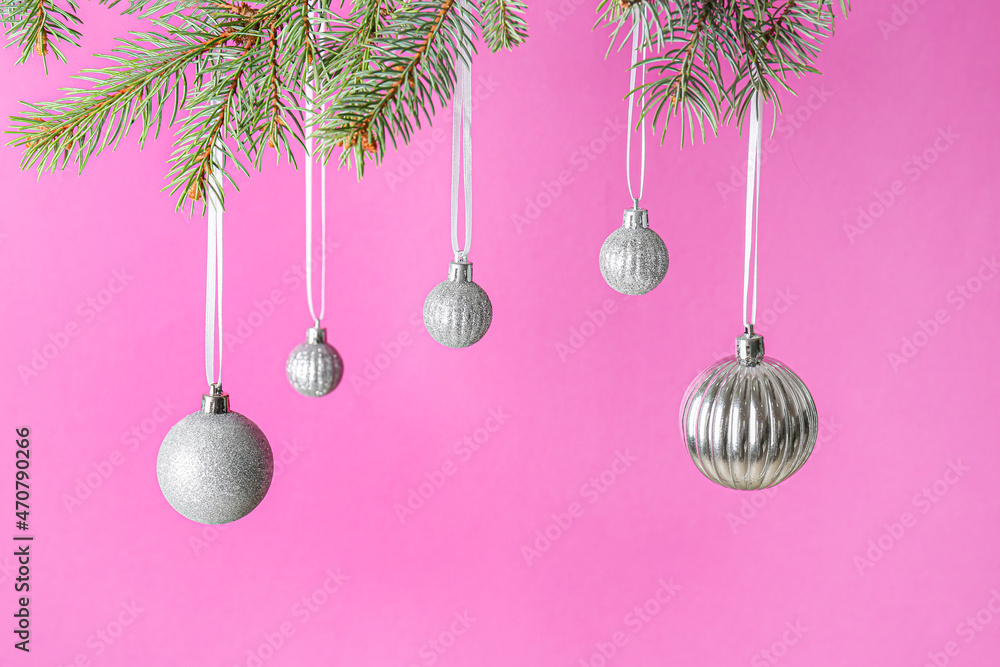 Different Christmas balls hanging on fir branches against color background