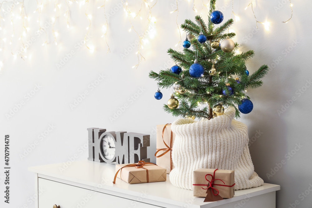 Small Christmas tree with gifts and clock on shelf near light wall