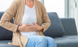 © JU.STOCKER - Unhappy woman stomach ache, mature woman with stomach pain feeling unwell sitting in living room