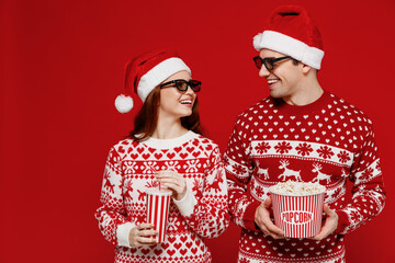 Wall Mural - Young fun couple friend man woman in 3d glasses watch movie film hold bucket of popcorn cup of soda pop look to each other isolated on plain red background People emotions in cinema lifestyle concept