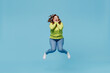 © ViDi Studio - Young overjoyed fun excited surprised chubby overweight plus size big fat fit woman wear green sweater jump high hold face isolated on plain blue background studio portrait. People lifestyle concept