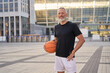 © Kostiantyn - Active middle aged man in sportswear looking at camera, standing outdoors with basketball ball, ready for workout in the city