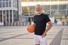 Active Middle Aged Man In Sportswear Looking At Camera, Standing Outdoors With Basketball Ball, Ready For Workout In The City