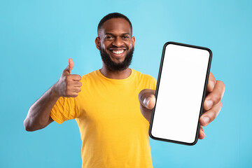 Black guy demonstrating cellphone with empty screen, showing thumb up, recommending website, offering space for mockup